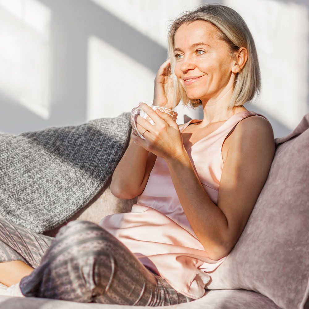Frau schaut lächelnd mit einer Tasse in der Hand